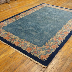 Low-pile rug in dusty blue with a floral center and decorative coral border on wood floors.
