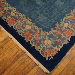 Corner of a blue floral rug with tan and rust borders on wide plank wood flooring.