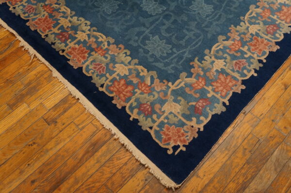 Corner of a blue floral rug with tan and rust borders on wide plank wood flooring.