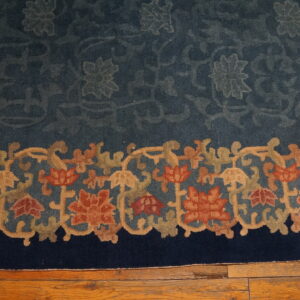Deep blue rug with a dense border of rust, olive, and tan florals resting on hardwood flooring.