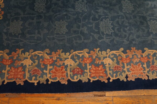 Deep blue rug with a dense border of rust, olive, and tan florals resting on hardwood flooring.