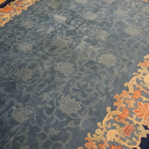 Muted blue rug features tone-on-tone floral designs and a coral, tan, and dark blue ornate border on wood floors.