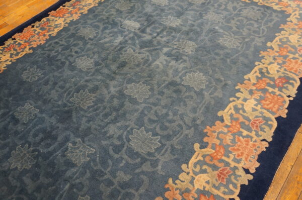 Muted blue rug features tone-on-tone floral designs and a coral, tan, and dark blue ornate border on wood floors.