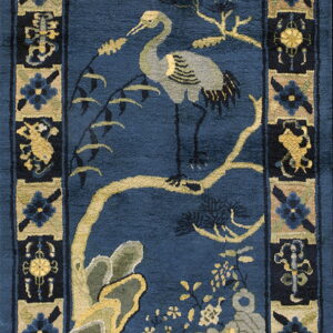 A vertical rug with a navy blue field, centered by a crane, tree, and rocks, surrounded by floral borders.