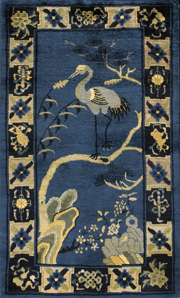 A vertical rug with a navy blue field, centered by a crane, tree, and rocks, surrounded by floral borders.