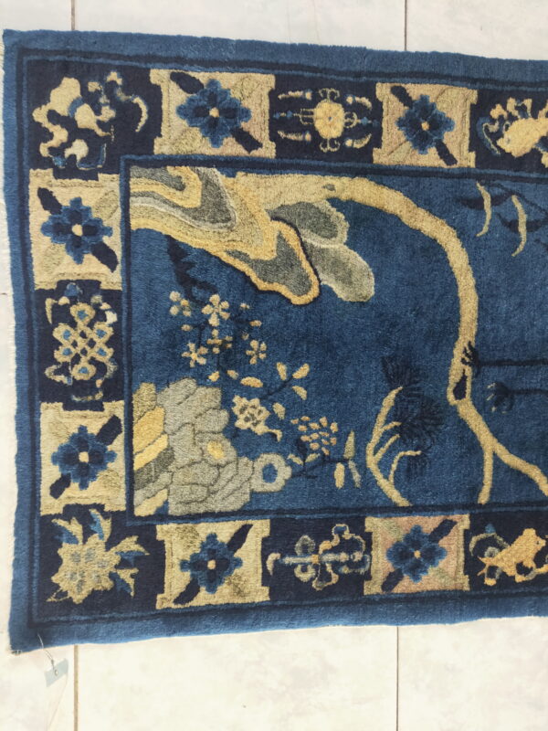 High-pile blue rug featuring yellow and gray floral patterns within a bordered design shown on white tile.