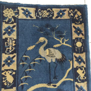 Blue rug with a tan crane and branch motif, framed by alternating dark blue and tan floral panels.
