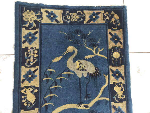 Blue rug with a tan crane and branch motif, framed by alternating dark blue and tan floral panels.