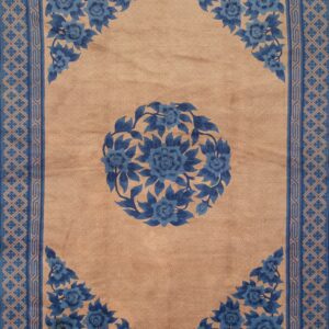 A beige rug with a blue floral medallion and ornate geometric borders lies on wide plank wood flooring.