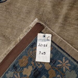 High-pile tan rug surface and fringe folded over the blue and khaki patterned woven backing.