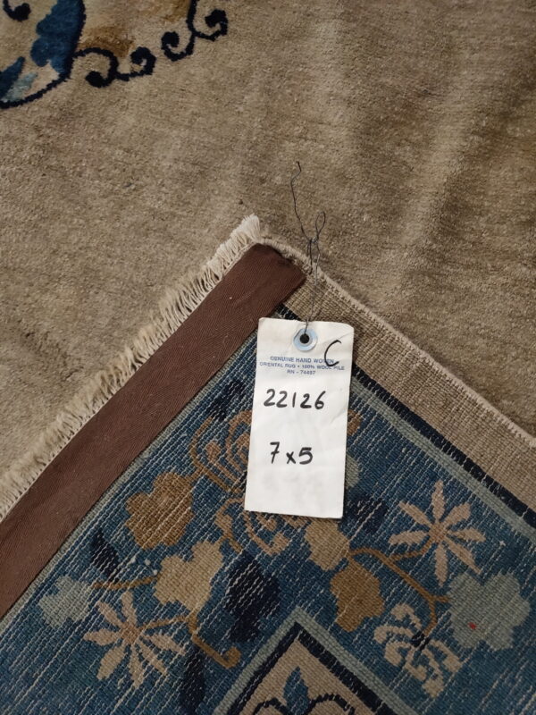 High-pile tan rug surface and fringe folded over the blue and khaki patterned woven backing.