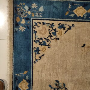 Beige rug with teal and gold floral border shown on white tile next to a brown shoe.