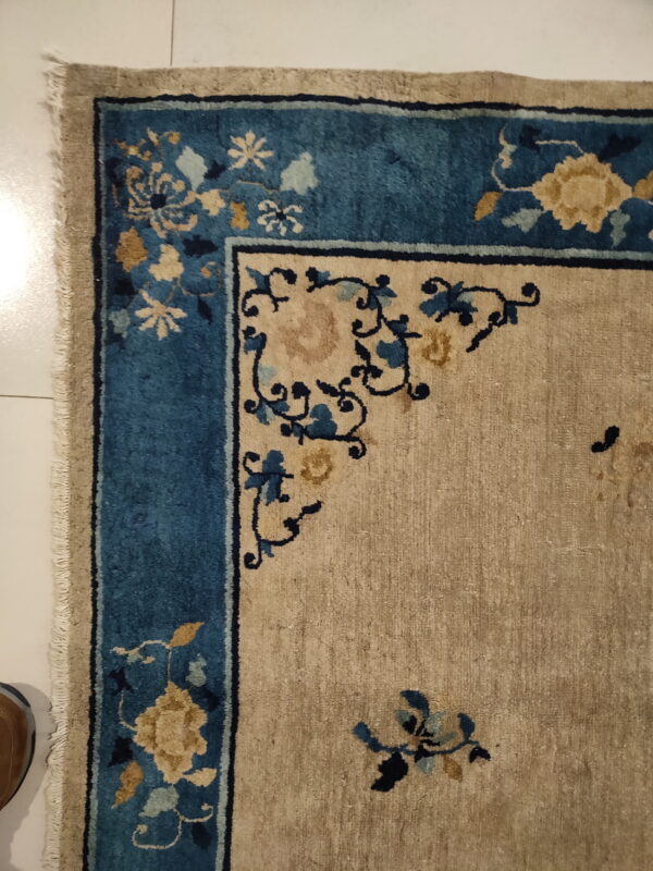 Beige rug with teal and gold floral border shown on white tile next to a brown shoe.
