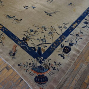 Corner view of a beige rug with a deep blue border and detailed botanical motifs on distressed wood.