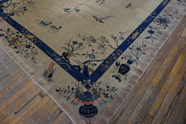 Corner view of a beige rug with a deep blue border and detailed botanical motifs on distressed wood.