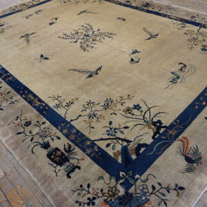 Tan low-pile rug with a wide blue border and detailed floral and flying bird patterns covers a wood floor.