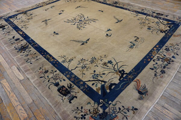 Tan low-pile rug with a wide blue border and detailed floral and flying bird patterns covers a wood floor.
