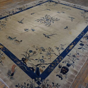 Beige rug with blue floral patterns and birds rests on worn, diagonal hardwood plank flooring.