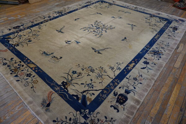 Beige rug with blue floral patterns and birds rests on worn, diagonal hardwood plank flooring.