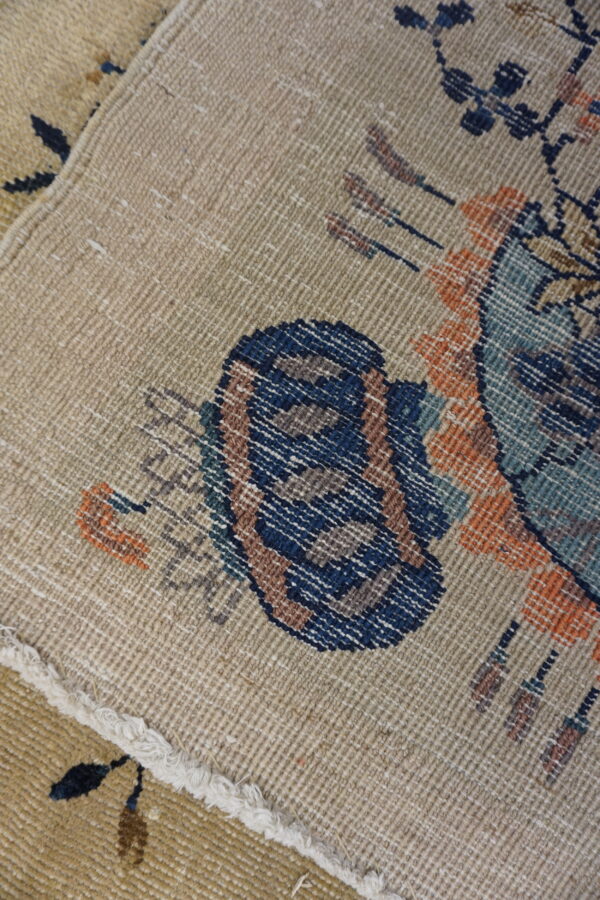 Beige, low-pile rug detail showing tightly woven dark blue, rust, and teal patterned elements.