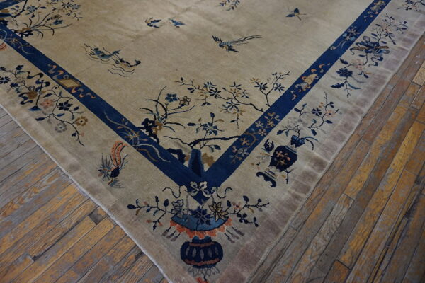 Tan rug with indigo blue borders and scattered floral and bird motifs covers distressed wood flooring.