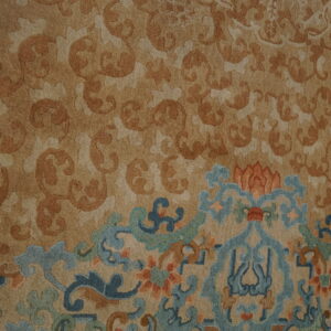 Close-up of a tan rug with tone-on-tone scrolling patterns and a colorful blue, green, and orange border.