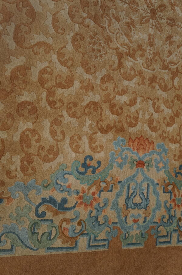 Close-up of a tan rug with tone-on-tone scrolling patterns and a colorful blue, green, and orange border.