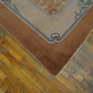 A beige and brown floral bordered rug rests on distressed wood plank flooring.