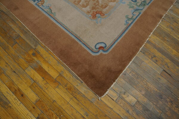A beige and brown floral bordered rug rests on distressed wood plank flooring.