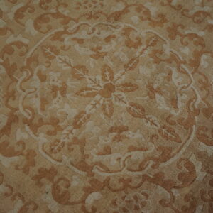 Beige and light brown rug detail showing an ornate classical design with a central floral medallion.