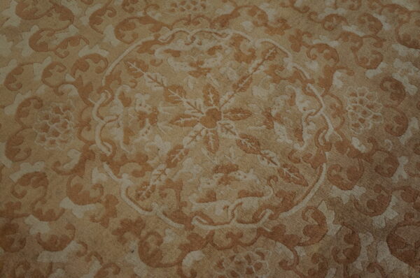 Beige and light brown rug detail showing an ornate classical design with a central floral medallion.