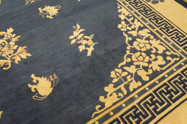 The rug has a navy blue field, yellow floral designs, and a complex key pattern border.