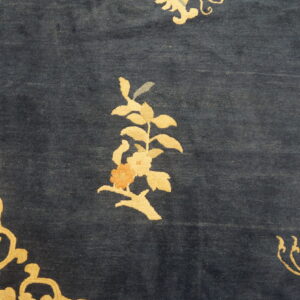 Detail of a navy blue rug with golden yellow floral sprigs and small peach and gray accent colors.