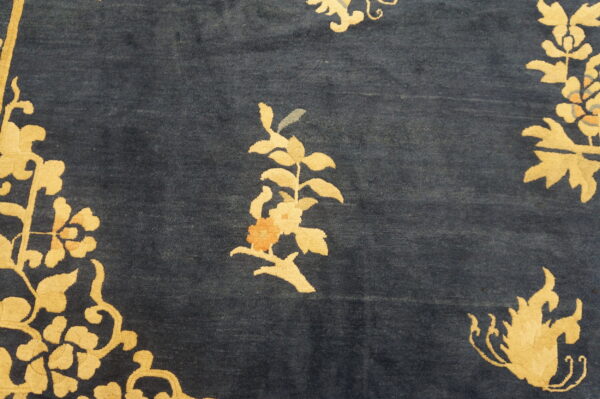 Detail of a navy blue rug with golden yellow floral sprigs and small peach and gray accent colors.