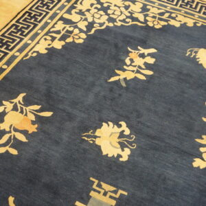 A closeup shows a navy rug with beige and light orange floral motifs and Greek key border details.