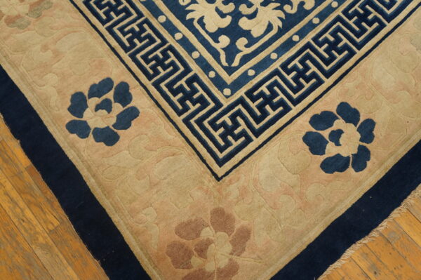 Navy and tan high-pile rug with geometric and carved floral patterns visible on worn wooden floorboards.