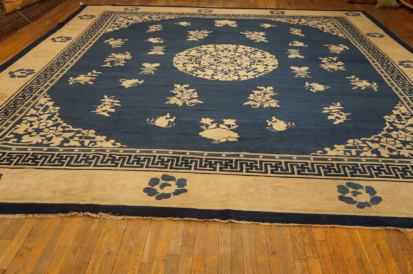 Large blue rug featuring scattered cream floral motifs, a central medallion, and a geometric border on wood floors.