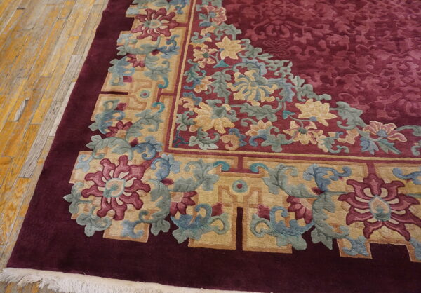 Deep burgundy rug corner with sculpted gold and floral patterns rests on distressed yellow wood flooring.