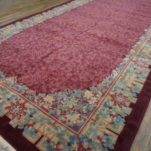 A long rug features a deep reddish-purple field bordered by intricate blue, tan, and gold florals on wood flooring.