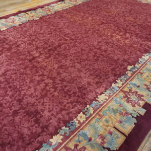 Low-pile maroon rug featuring a sculpted floral pattern and ornate multicolored borders on rustic wood flooring.