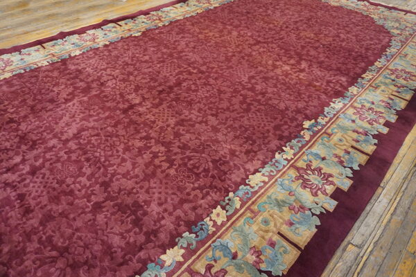 Low-pile maroon rug featuring a sculpted floral pattern and ornate multicolored borders on rustic wood flooring.