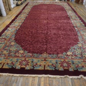 Oversized burgundy rug with a sculpted floral field and complex gold, blue, and pink carved borders.
