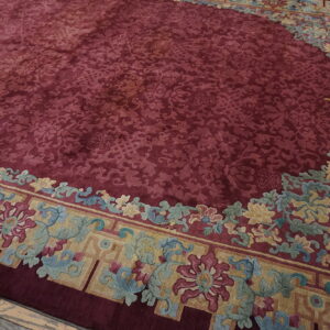 Deep red rug with complex tone-on-tone pattern, bordered by colorful florals in gold, blue, and magenta.