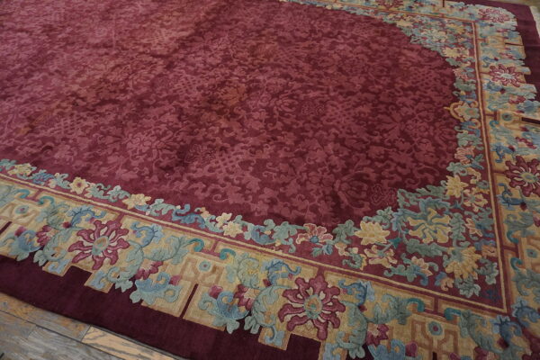 Deep red rug with complex tone-on-tone pattern, bordered by colorful florals in gold, blue, and magenta.