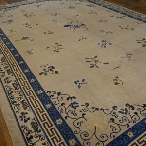The beige rug has scattered blue and brown botanical motifs and an ornate blue border on wood planks.