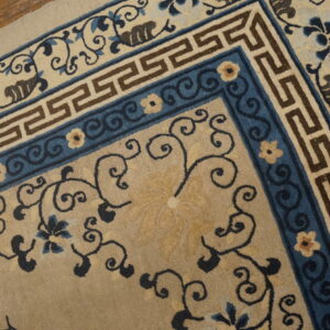Medium pile rug detail showing tan, blue, and brown borders with Greek key and scrolling florals on wood floor.