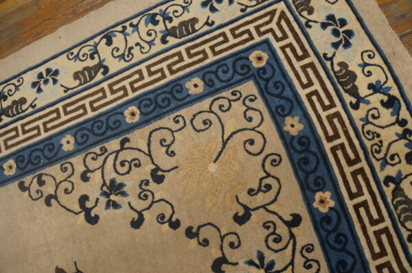 Medium pile rug detail showing tan, blue, and brown borders with greek key and scrolling florals on wood floor.