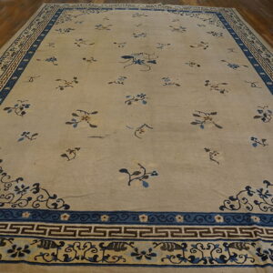 Large beige rug with scattered blue floral motifs and a detailed blue key-patterned border on wood flooring.