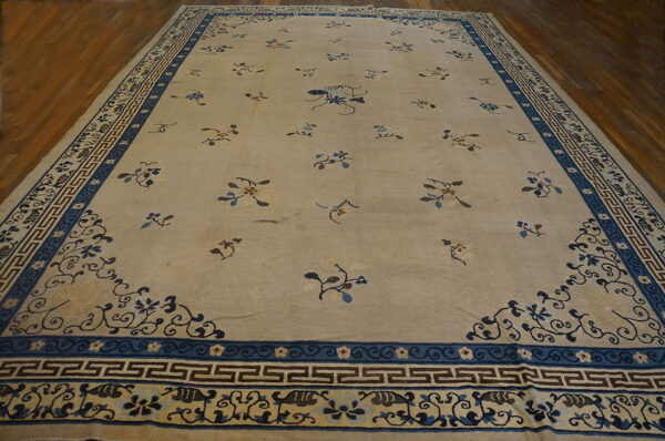 Large beige rug with scattered blue floral motifs and a detailed blue key-patterned border on wood flooring.