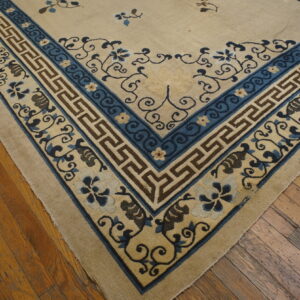 The corner of a cream and blue rug with geometric and floral patterns sits on rustic wood flooring.
